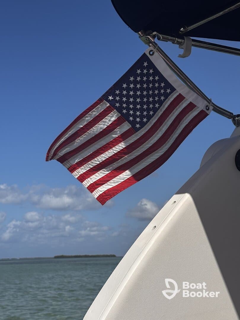 A close-up of an American flag waving on a boat against a clear blue sky, showcasing the vessel's patriotic spirit while cruising on the water.