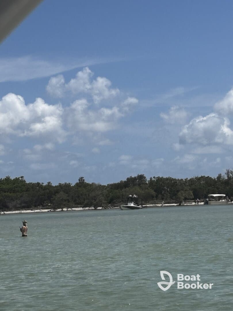 A person stands in shallow water while a boat is anchored nearby, capturing a serene fishing moment in a picturesque setting.