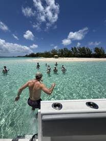 A group of friends enjoys a fun day at the beach, splashing in the clear waters while one person jumps in from the boat — perfect for a memorable day on the water.