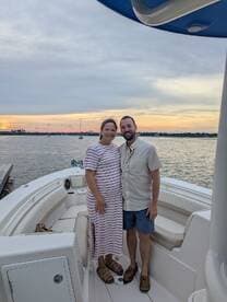 A couple poses for a photo on their boat at sunset, capturing a moment of joy and celebration on the water.