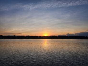 A stunning sunset casts vibrant colors over the water, creating a picturesque scene perfect for evening boat cruises or relaxation by the shore.