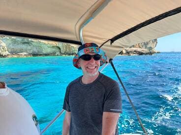 A cheerful man enjoys a sunny day on the boat, surrounded by stunning turquoise waters and rocky cliffs — perfect for a memorable boating adventure.