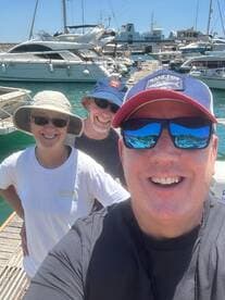 A cheerful group of friends poses for a selfie at the marina, surrounded by boats — capturing the joy of a day on the water.