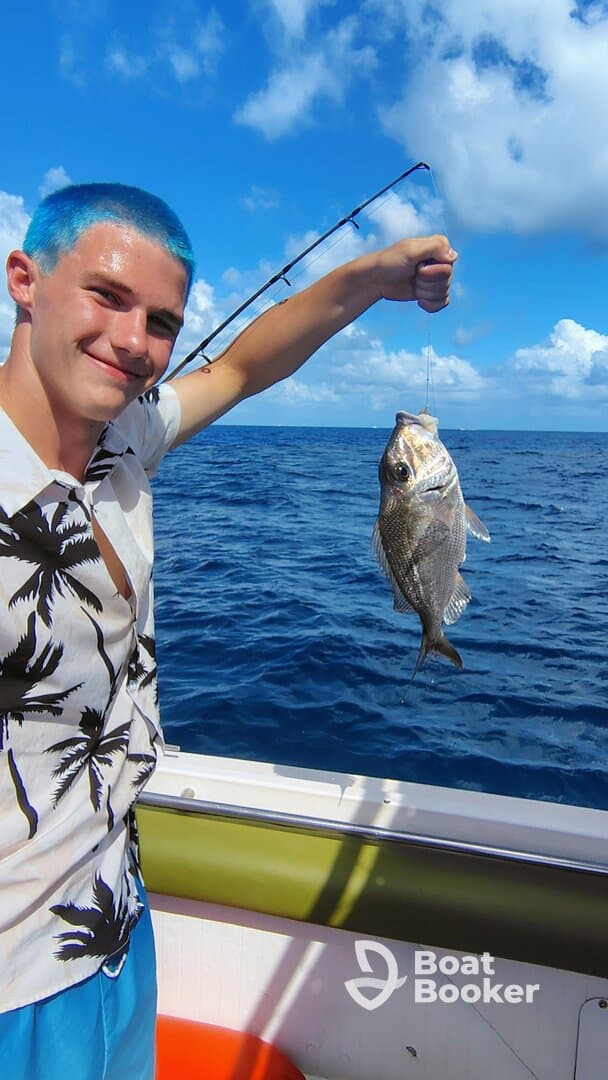 A young man proudly displays his catch while fishing in the open ocean, showcasing the thrill of a successful day on the water.