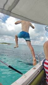 A young boy leaps off the side of a boat into the clear turquoise waters, capturing the thrill of summer fun and on-water adventures.