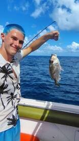 A young man proudly displays his catch while fishing in the open ocean, showcasing the thrill of a successful day on the water.