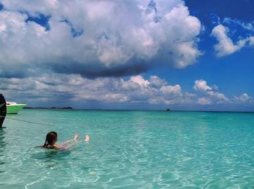 A person enjoys a refreshing swim in crystal-clear waters, with a boat anchored nearby, showcasing the beauty of a tropical getaway.