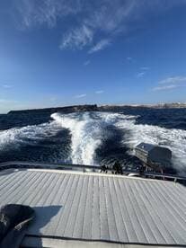 A sleek boat cuts through the waves, showcasing its design against a backdrop of clear blue skies and distant cliffs — perfect for adventure seekers on the water.
