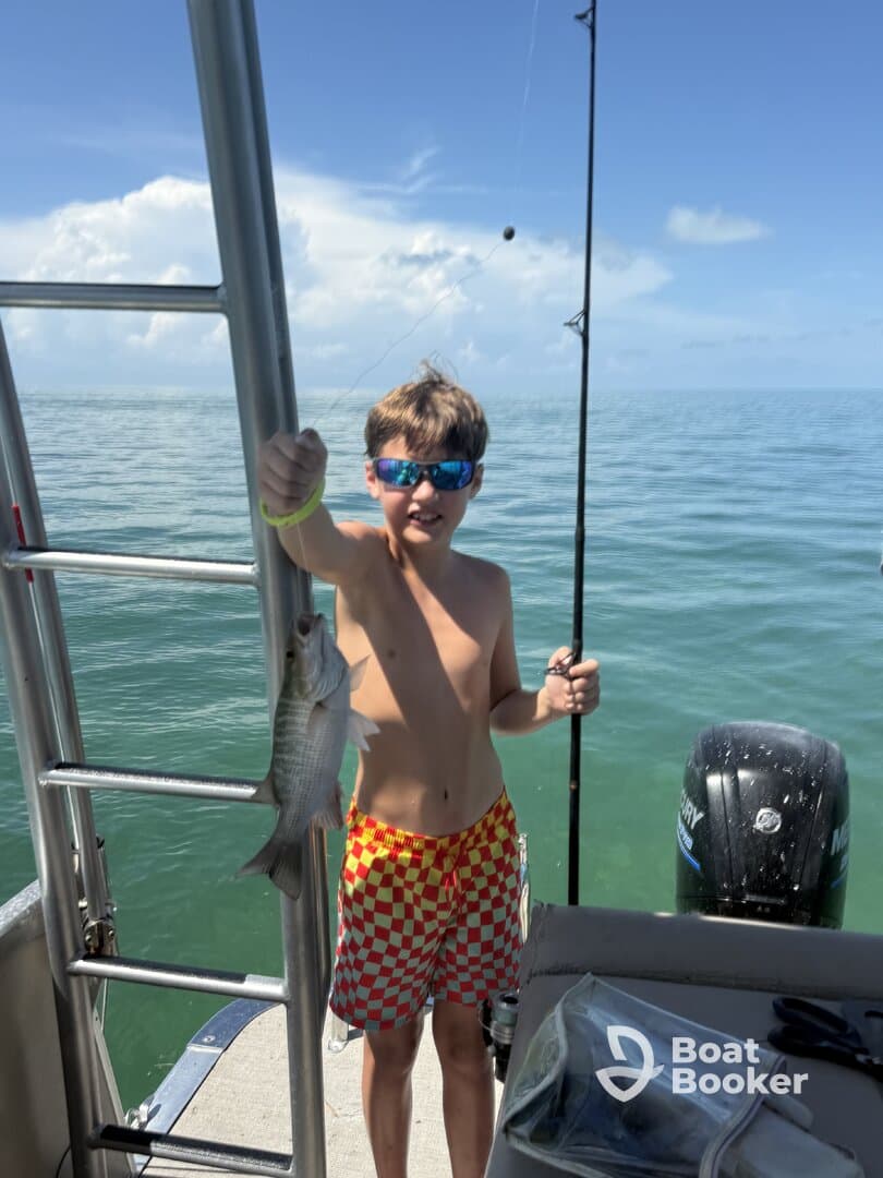 A young boy proudly holds up his catch while fishing on a boat, showcasing the excitement of a day on the water.