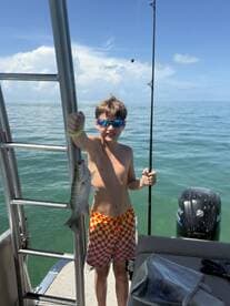 A young boy proudly holds up his catch while fishing on a boat, showcasing the excitement of a day on the water.