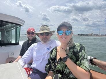 A cheerful group enjoys a sunny day on the water, capturing memories aboard their boat with a scenic pier in the background.