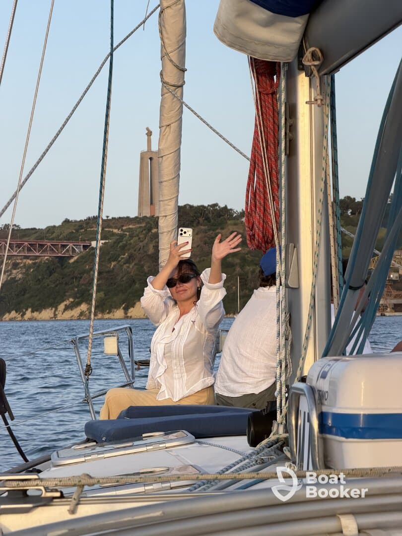 A woman enjoys a moment on a sailboat, capturing the experience with her phone as the scenic backdrop enhances the joyful atmosphere of the sailing trip.