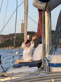 A woman enjoys a moment on a sailboat, capturing the experience with her phone as the scenic backdrop enhances the joyful atmosphere of the sailing trip.