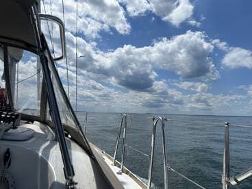 A serene view from the deck of a sailboat, showcasing the calm waters and expansive sky, perfect for a peaceful day on the water.