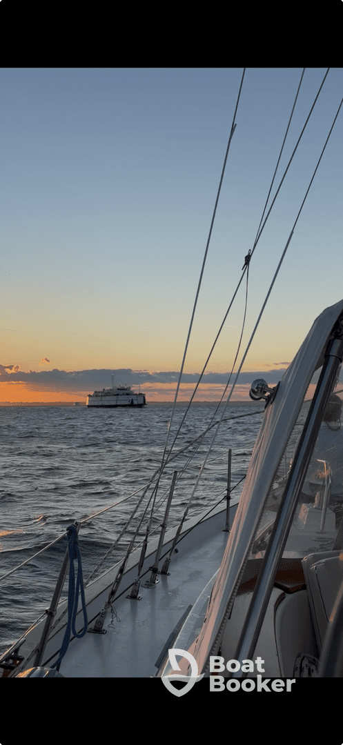 A serene view of a sailboat navigating through calm waters at sunset, with another vessel visible in the distance, creating a picturesque maritime scene.