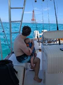 A father holds his baby on a fishing boat, enjoying a beautiful day on the ocean — a perfect family moment amidst the serene waters.