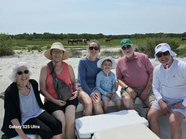 A joyful family gathers on a boat at the beach, with wild horses grazing in the background — a perfect moment of togetherness and adventure.