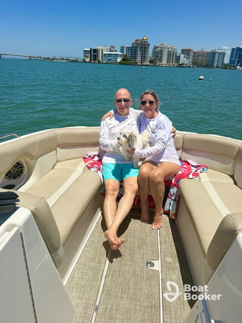 A couple enjoys a sunny day on their boat with a dog, showcasing a perfect moment of relaxation on the water against a vibrant city backdrop.