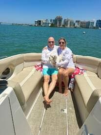 A couple enjoys a sunny day on their boat with a dog, showcasing a perfect moment of relaxation on the water against a vibrant city backdrop.