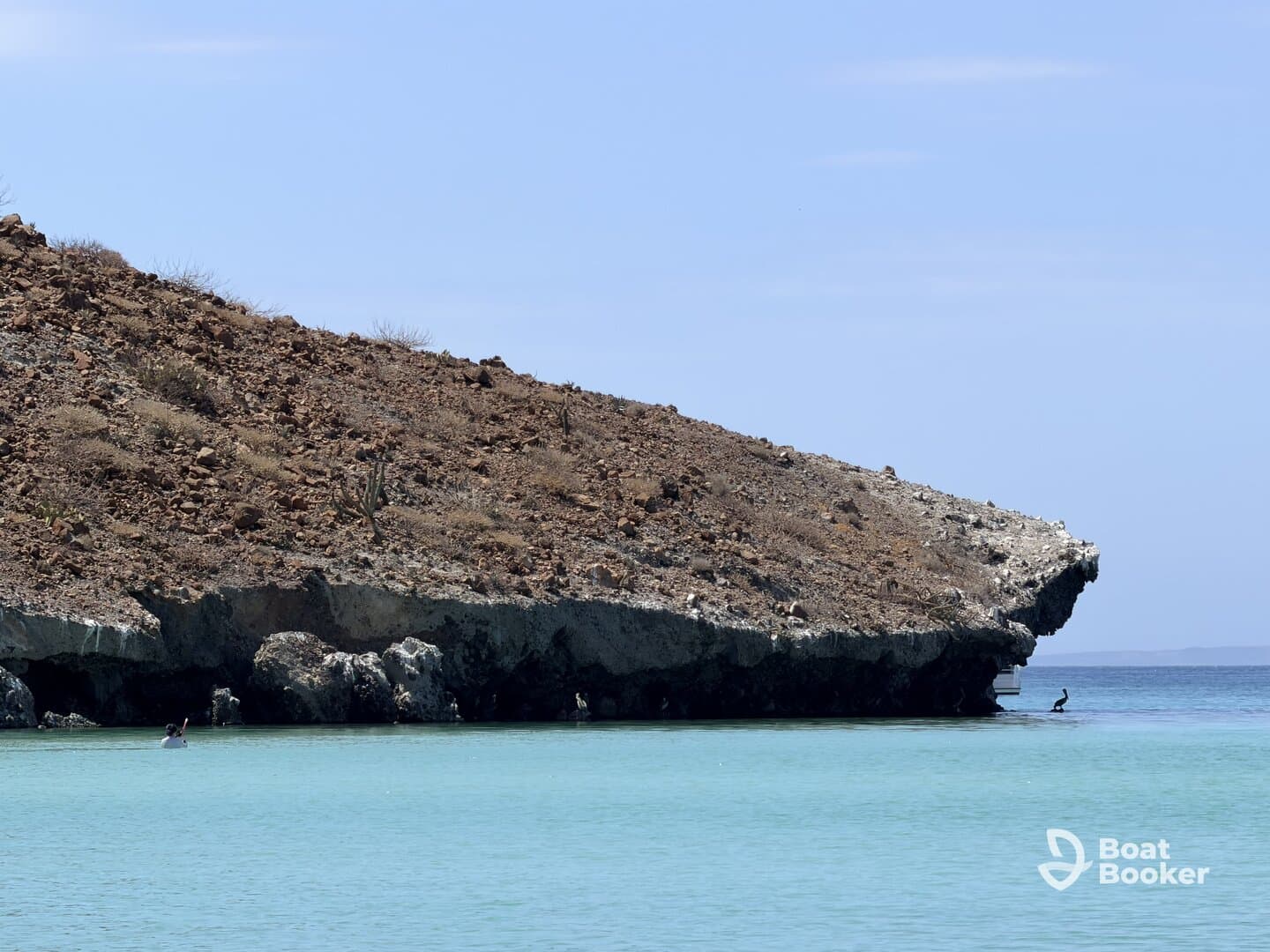 A serene view of a coastline with a person kayaking in the foreground, showcasing the beautiful turquoise waters and rocky landscape — perfect for adventure seekers and nature lovers.