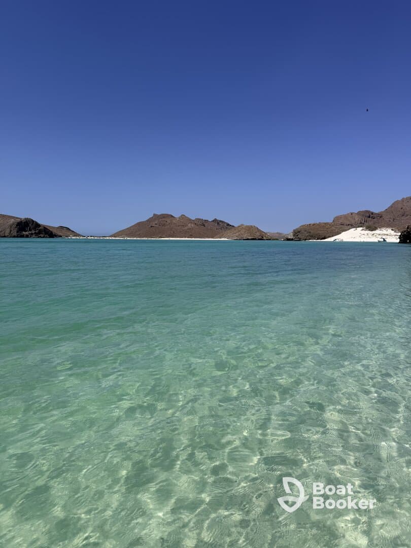 A stunning view of a tranquil beach with clear turquoise waters and rocky hills in the background, perfect for showcasing beautiful coastal destinations.