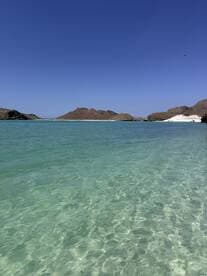 A stunning view of a tranquil beach with clear turquoise waters and rocky hills in the background, perfect for showcasing beautiful coastal destinations.
