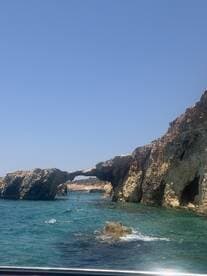 A stunning view of a natural rock arch along the coastline, with people enjoying the turquoise waters nearby — a perfect highlight of a boating adventure.