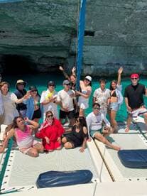A lively group poses for a fun photo aboard a catamaran, celebrating under the sun with stunning turquoise waters in the background — perfect for memorable outings and adventures.
