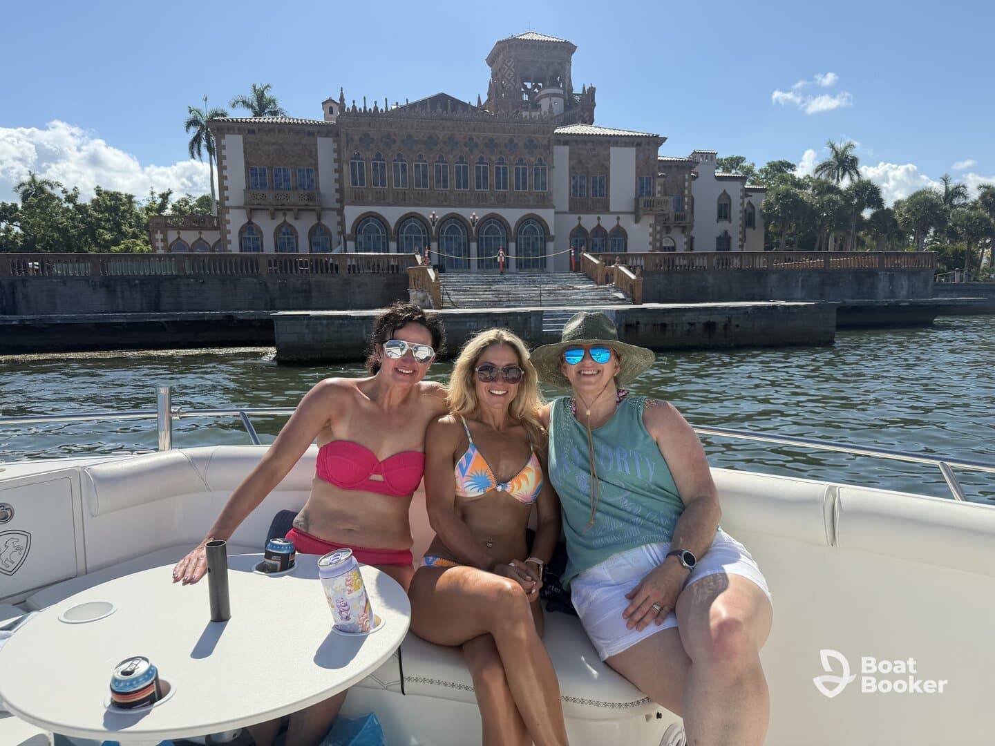 A group of friends enjoys a sunny day on the boat, with a stunning waterfront mansion in the background, perfect for memorable outings and celebrations.