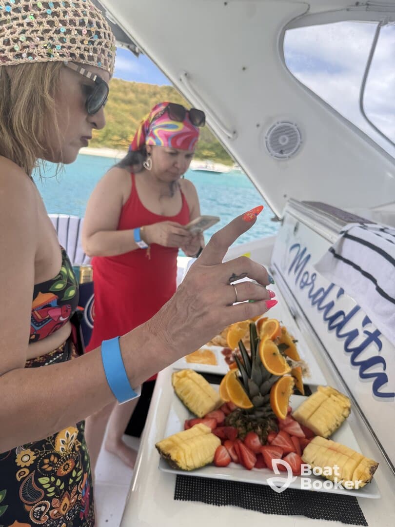 Two women enjoy a beautifully arranged fruit platter aboard a boat, perfect for refreshing snacks during a day on the water.