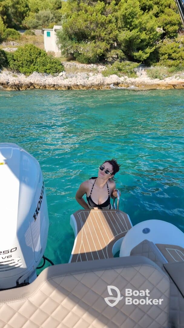 A woman enjoys a refreshing swim next to a boat in crystal-clear waters, perfect for summer adventures and relaxation on the water.