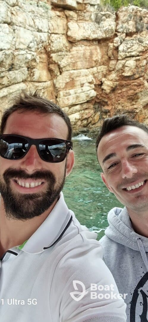 Two friends take a cheerful selfie while enjoying a boating adventure, surrounded by stunning rocky scenery — perfect for capturing memorable moments on the water.
