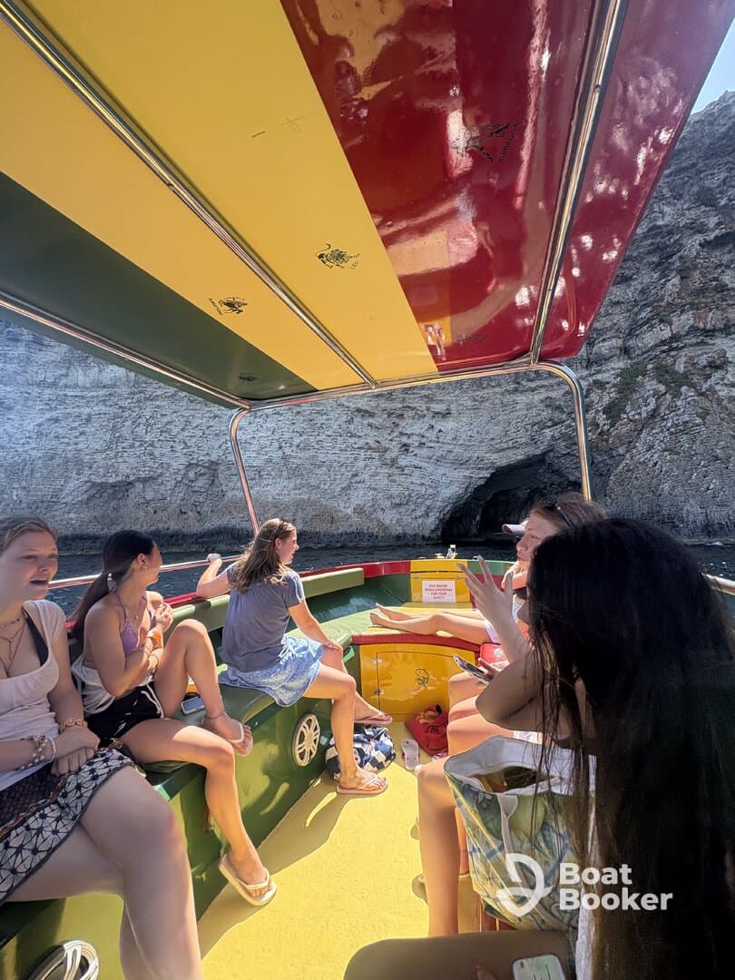 A lively group enjoys their time aboard a colorful boat, with a stunning cave backdrop — perfect for adventure and exploration on the water.