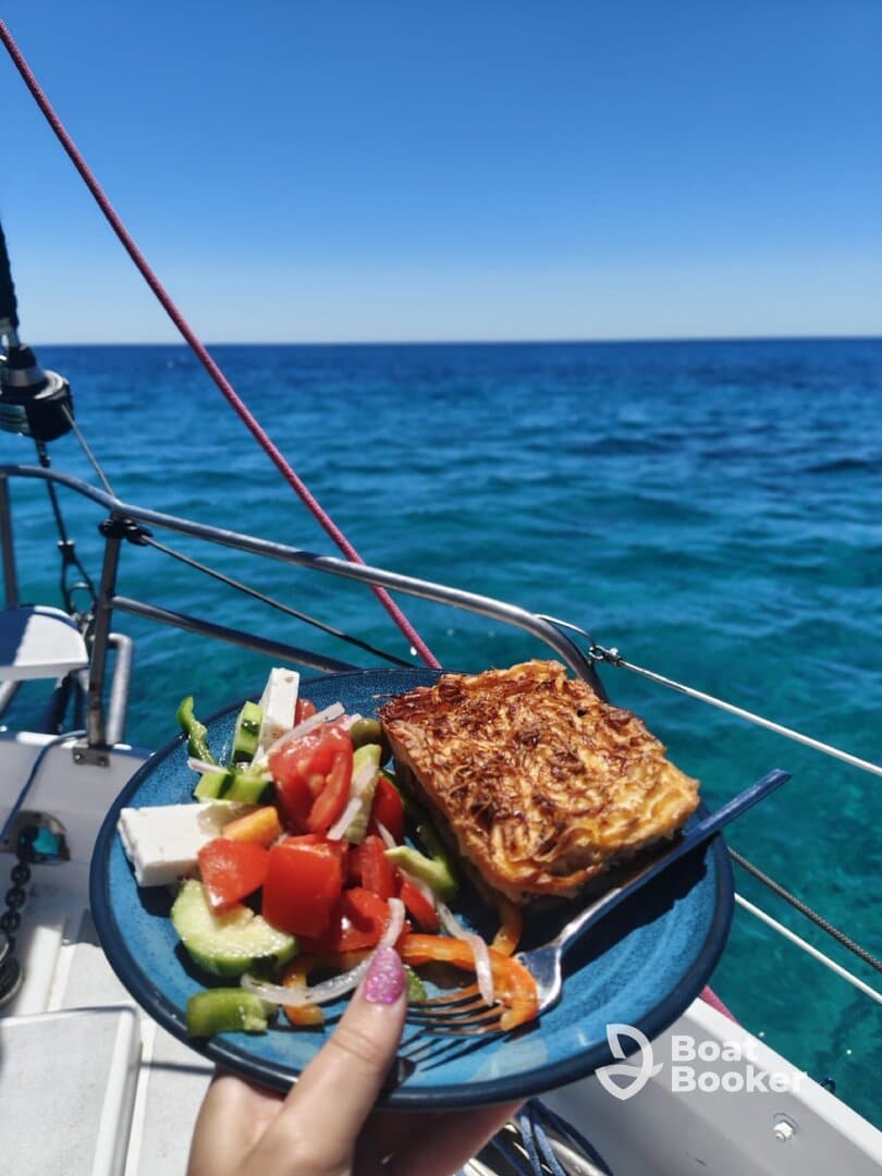 A delicious meal featuring a fresh salad and baked dish served on a plate while enjoying the beautiful ocean view from the boat — perfect for a relaxing day at sea.