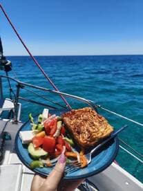 A delicious meal featuring a fresh salad and baked dish served on a plate while enjoying the beautiful ocean view from the boat — perfect for a relaxing day at sea.