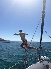 A person leaps off the bow of a boat into the sparkling blue waters, capturing the essence of summer fun and adventure on the water.