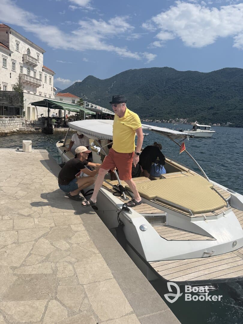 A lively scene at the dock with a group preparing to board a boat, set against a stunning mountainous backdrop — perfect for summer adventures on the water.