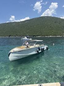 A speedboat is docked in clear waters with a scenic mountainous backdrop, showcasing its sleek design and inviting atmosphere for a day on the water.