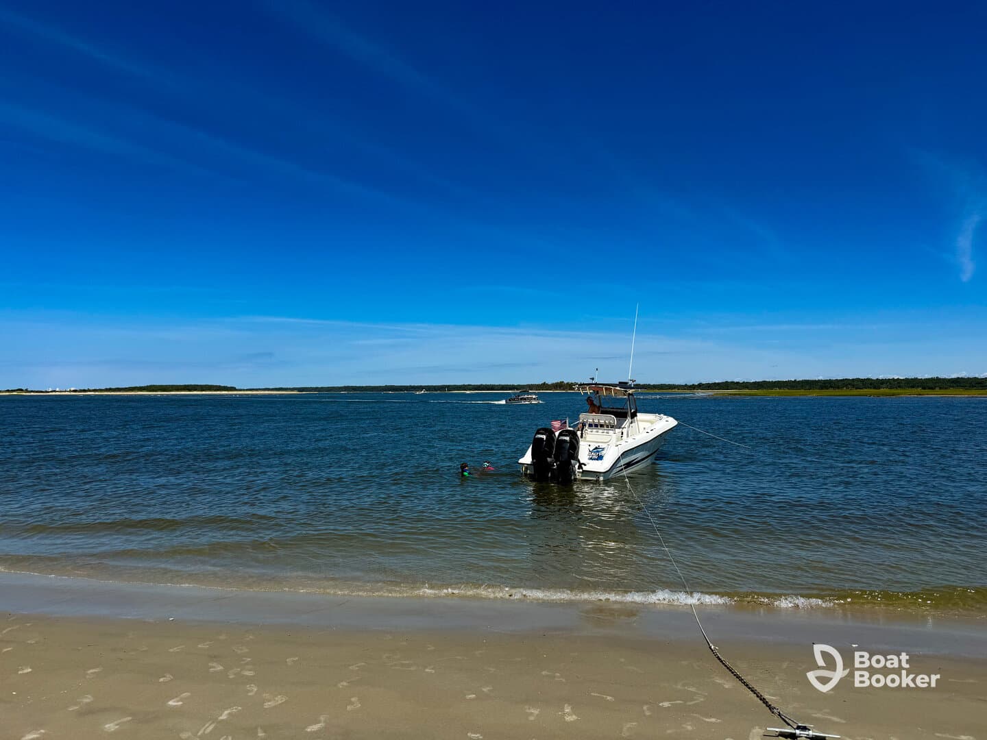 A boat is anchored near the beach with a person swimming nearby, showcasing a perfect day on the water.