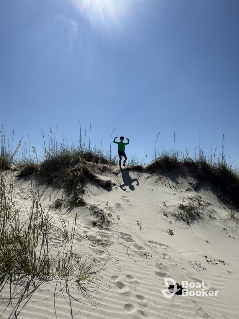 A child poses playfully on a sand dune under a bright sun, showcasing a fun day outdoors.