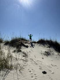 A child poses playfully on a sand dune under a bright sun, showcasing a fun day outdoors.