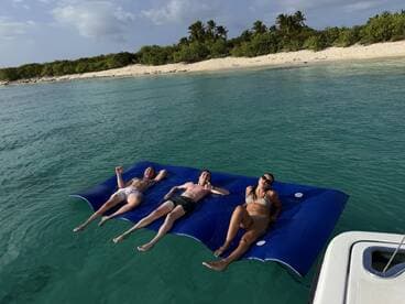 A group of friends relaxes on a floating mat in crystal-clear waters, enjoying a perfect day at the beach — ideal for sunbathing and fun in the sun.