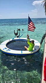 A lively group enjoys a fun day on the water, featuring a floating mat and snorkeling gear, perfect for family adventures in crystal-clear waters.
