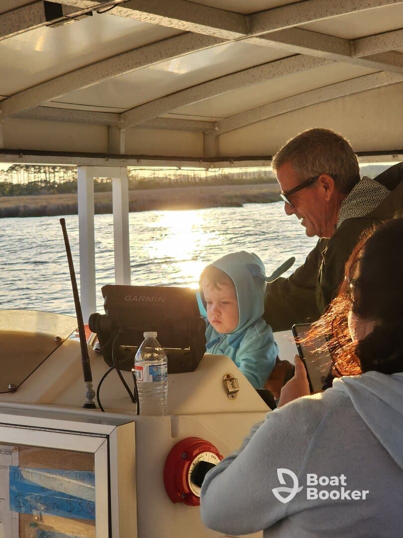 A heartwarming moment on a boat as a child and adult engage at the helm during sunset, capturing the joy of family time on the water.