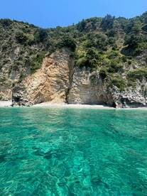 A stunning view of a rocky coastline with crystal-clear waters, showcasing a serene beach scene — perfect for exploring nature's beauty while boating.