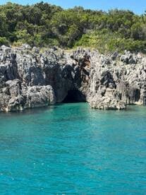 A stunning view of a rocky coastline featuring a cave entrance, surrounded by crystal-clear turquoise waters — a perfect destination for exploration and adventure.