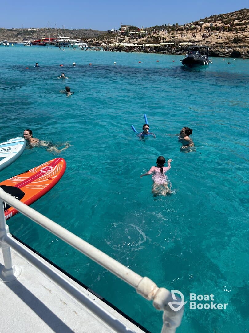 A lively scene of people enjoying a sunny day in crystal-clear waters, with children playing and adults swimming — perfect for family fun and water activities.
