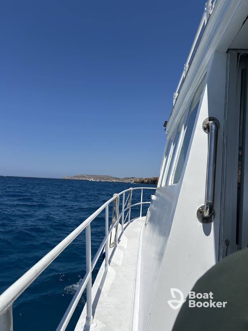 A clear view of the side of a boat cruising through vibrant blue waters, showcasing the vessel's structure against a sunny sky.