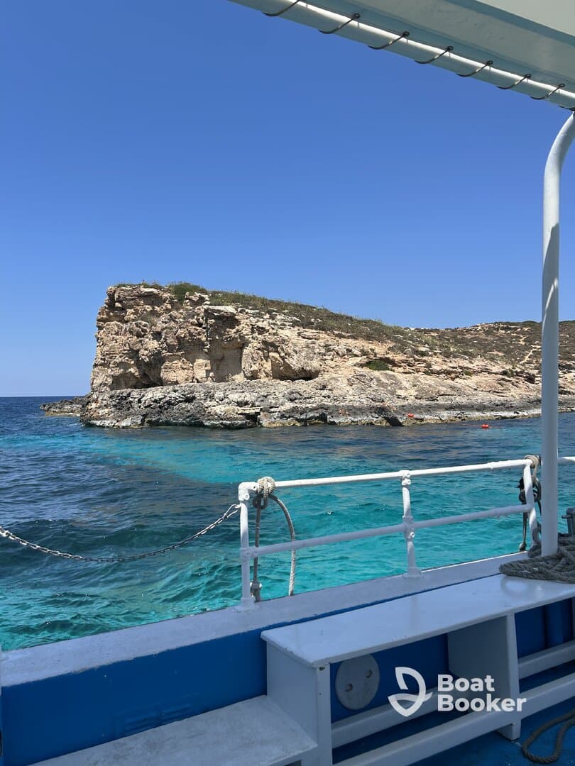 A stunning view of a rocky coastline from aboard a boat, showcasing the vibrant turquoise waters and clear blue skies — perfect for a day of exploration and adventure.