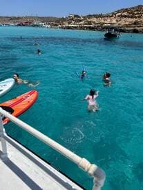 A lively scene of people enjoying a sunny day in crystal-clear waters, with children playing and adults swimming — perfect for family fun and water activities.